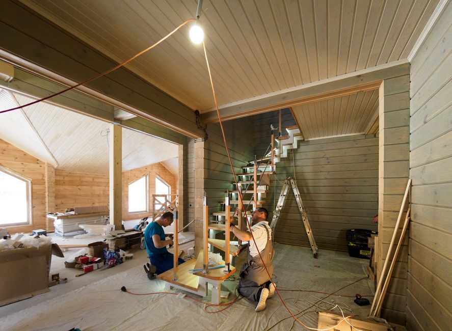 Two workers inside a residential property are engaged in the process of home relocation and furniture transport, specifically focusing on navigating a staircase. They are installing or securing a stai